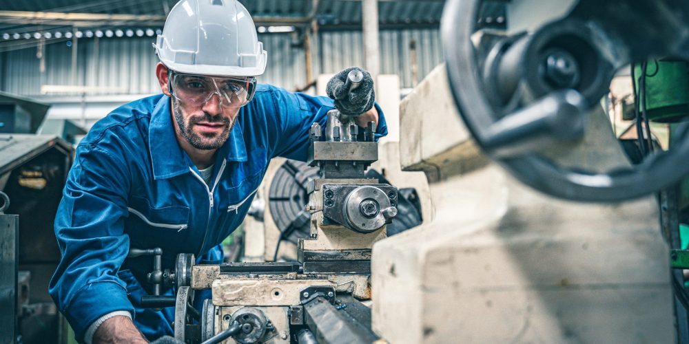 Male worker in blue jumpsuit and white hardhat operating lathe m