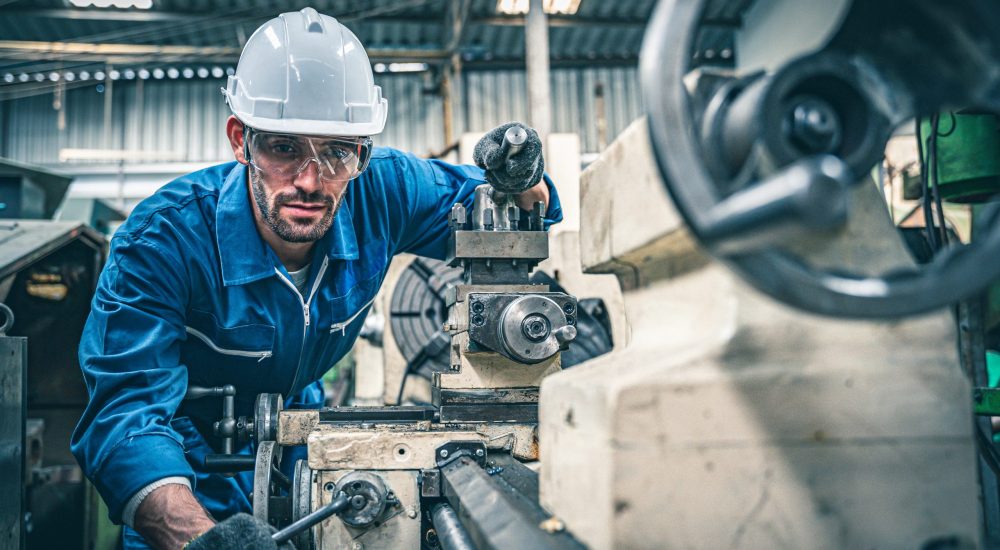 Male worker in blue jumpsuit and white hardhat operating lathe m