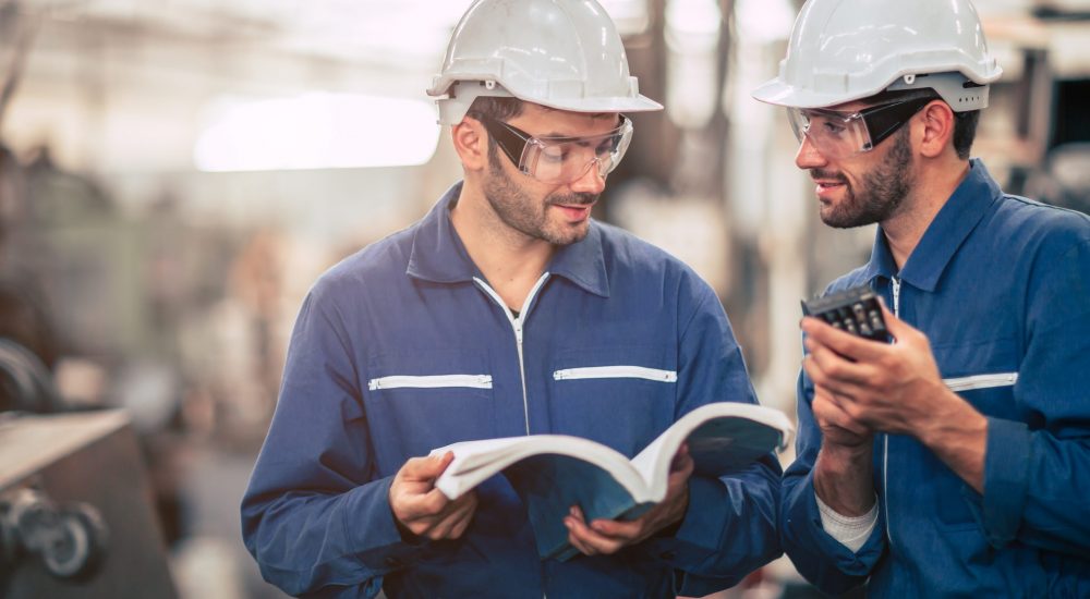 Engineer team talking together teach and learn egineering technical about using machine with open instruction manual text book in factory workplace.